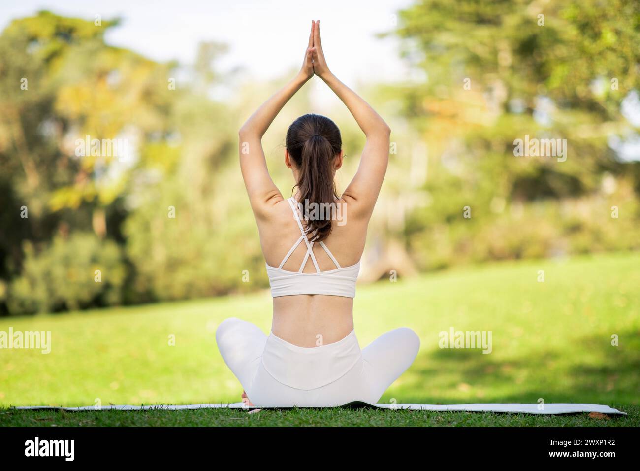 Viewed from behind, a woman in a seated yoga pose extends her arms ...