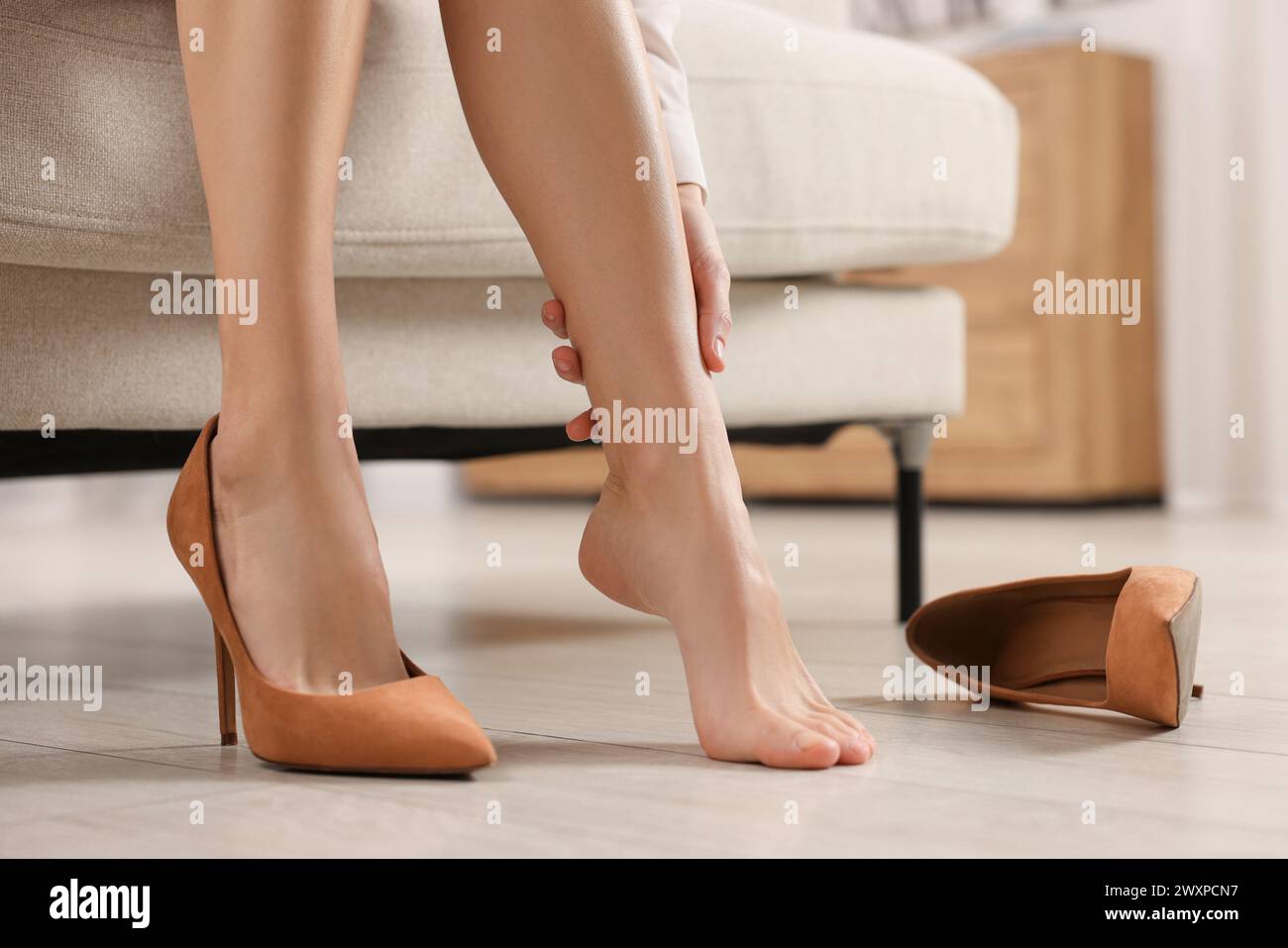 Woman suffering from leg pain after wearing high heels at home, closeup Stock Photo