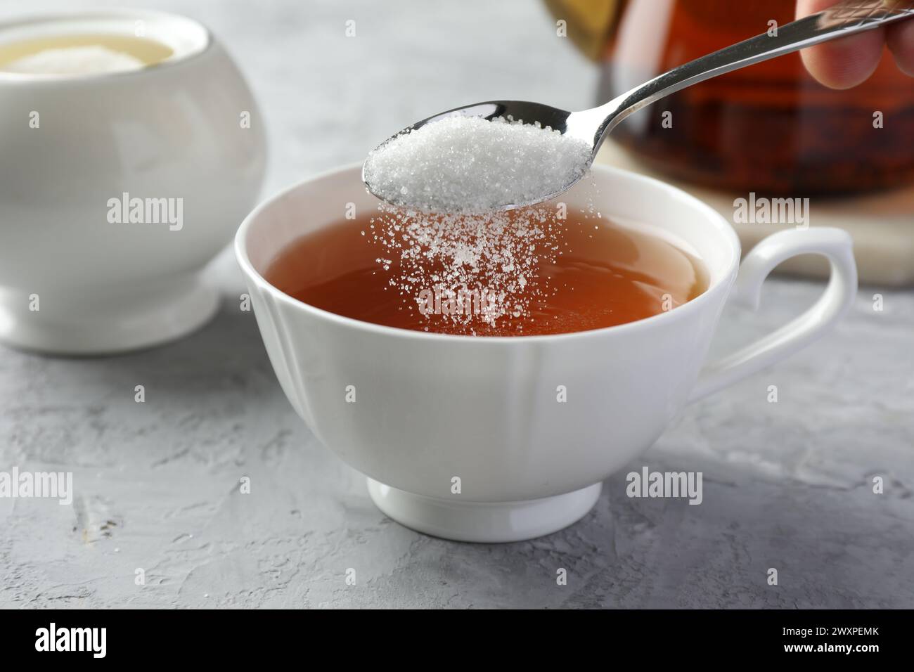 Adding sugar into cup of tea at grey textured table, closeup Stock ...