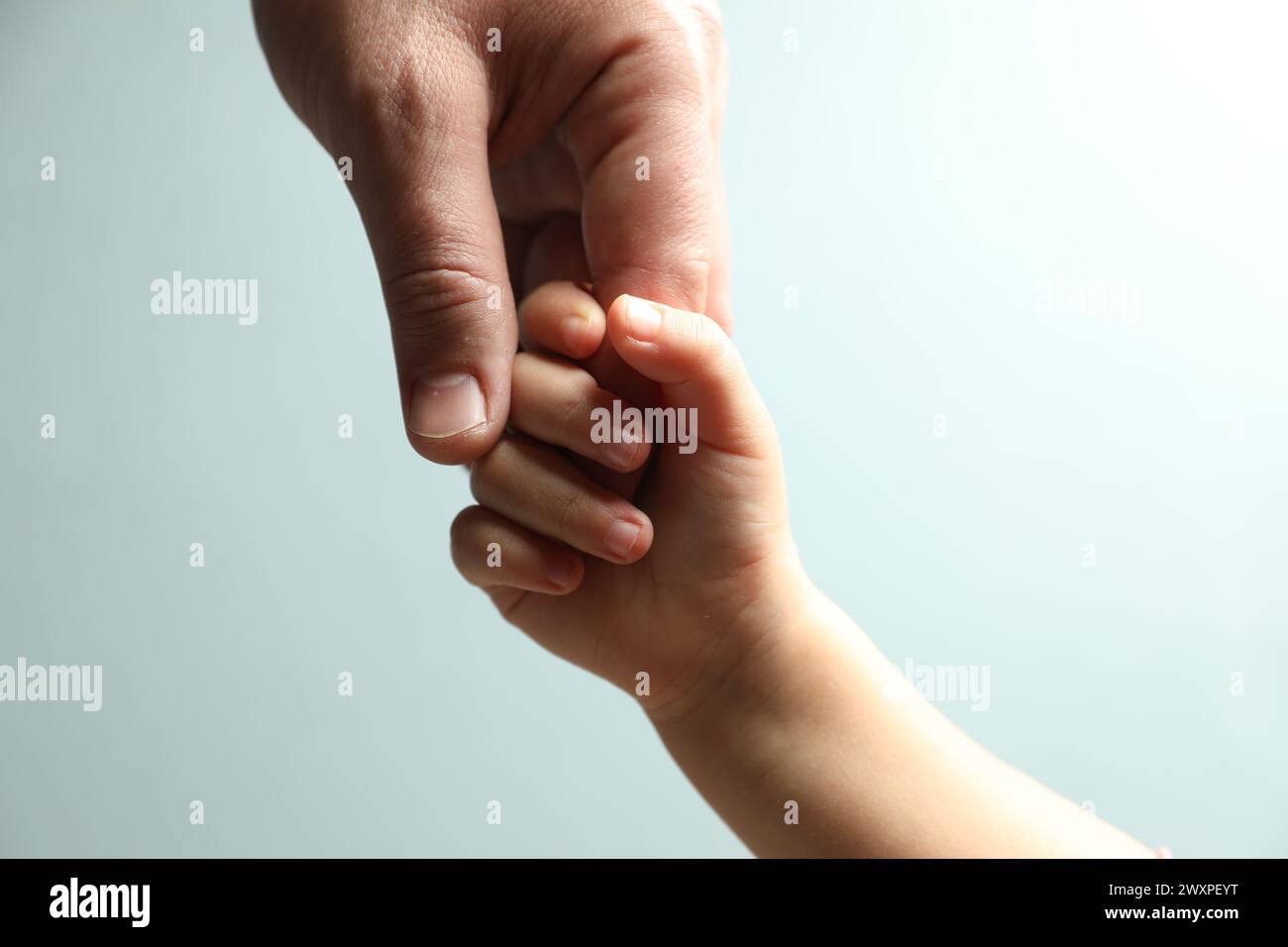 Father and child holding hands on light blue background, closeup Stock Photo