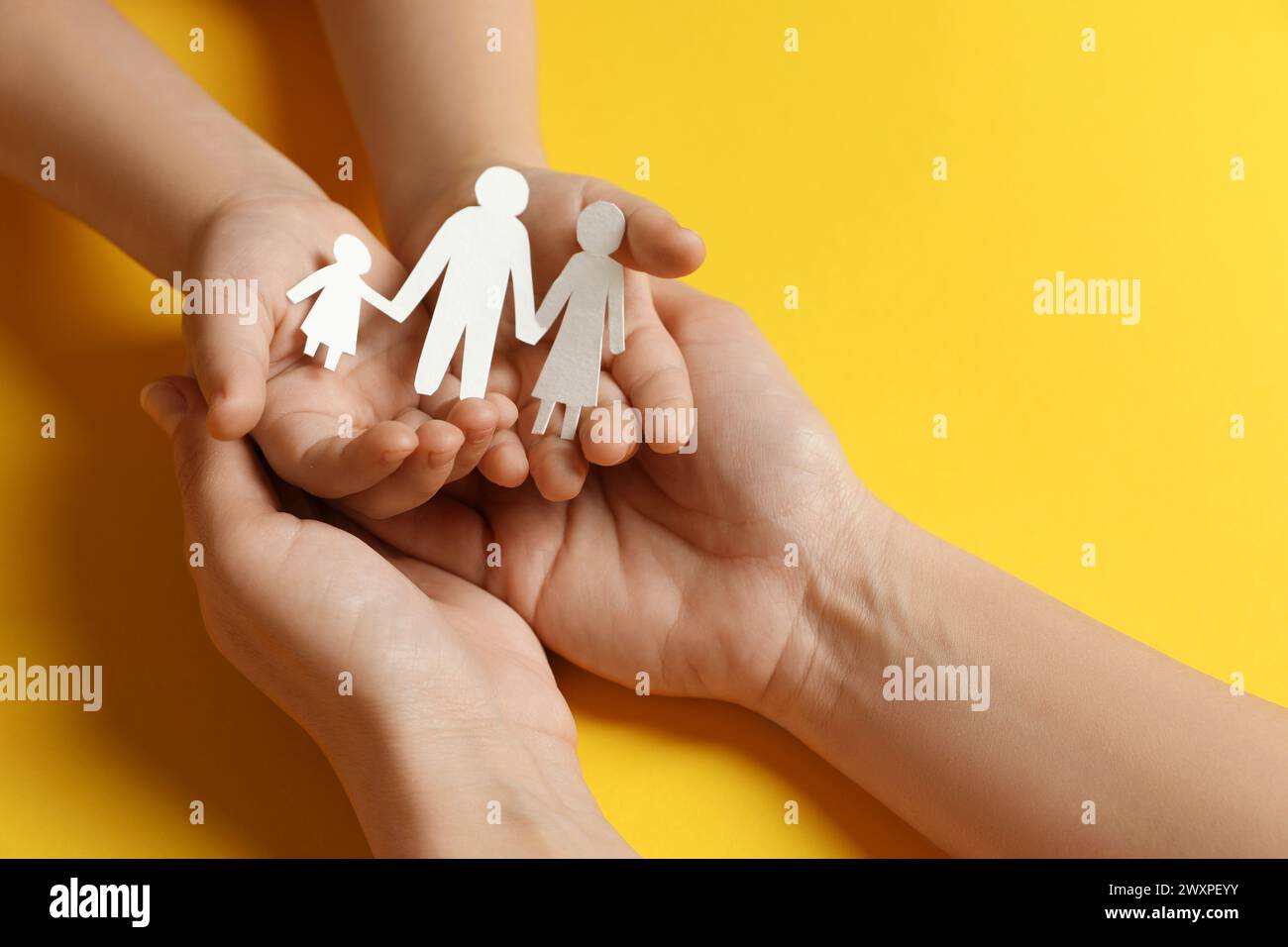 Mother and child holding paper cutout of family on yellow background, closeup Stock Photo