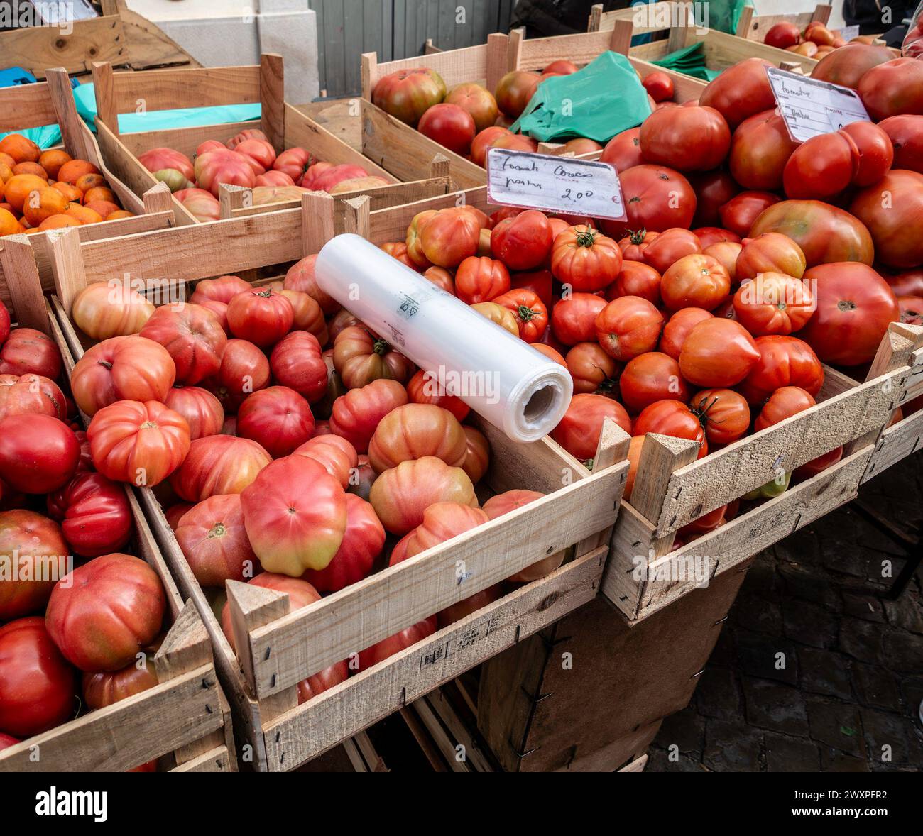 A variety of ripe heirloom tomatoes are neatly arranged in wooden crates, ready for customers to purchase in Loule, Portugal. Stock Photo