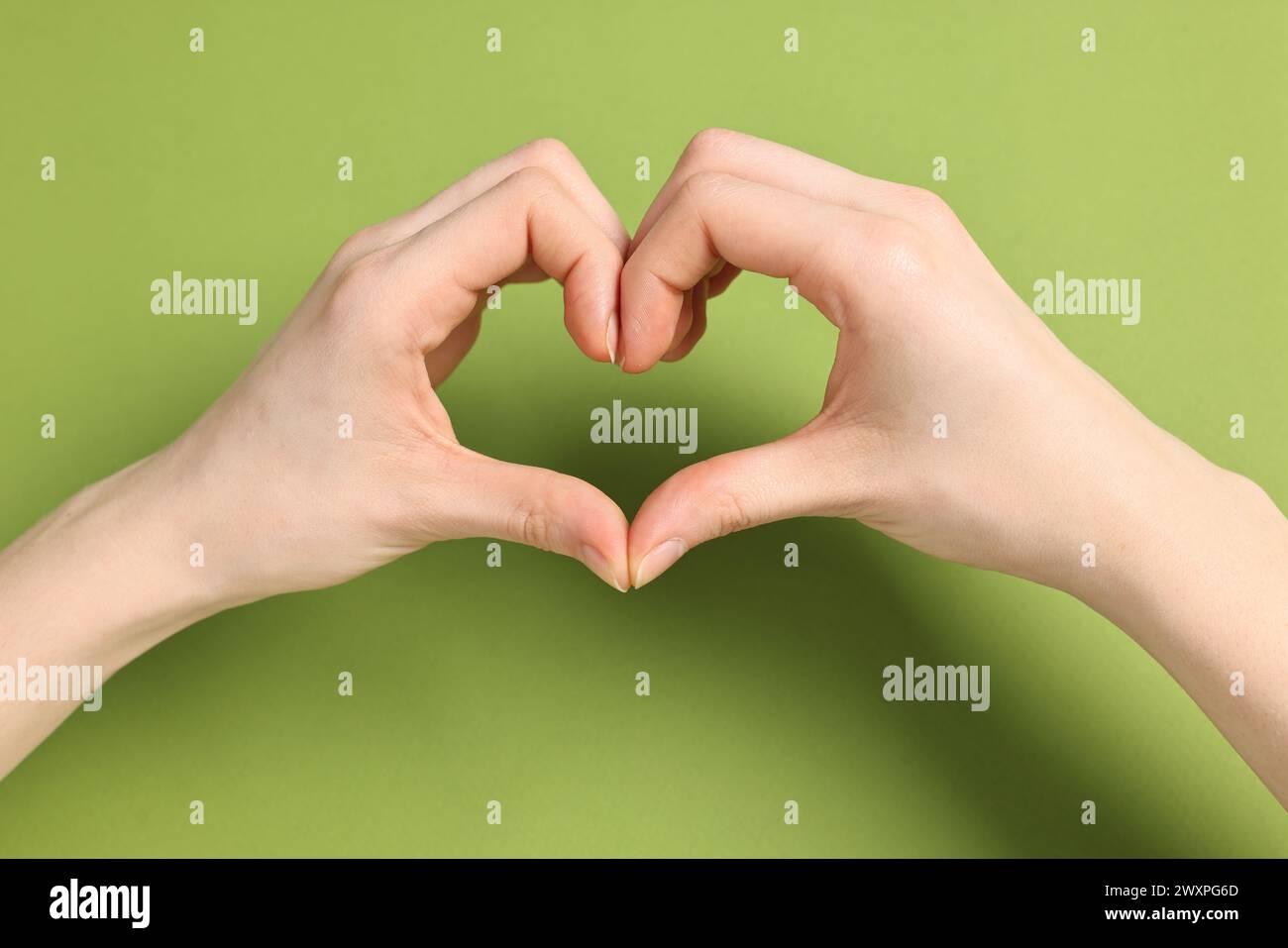 Woman showing heart gesture with hands on green background, closeup Stock Photo