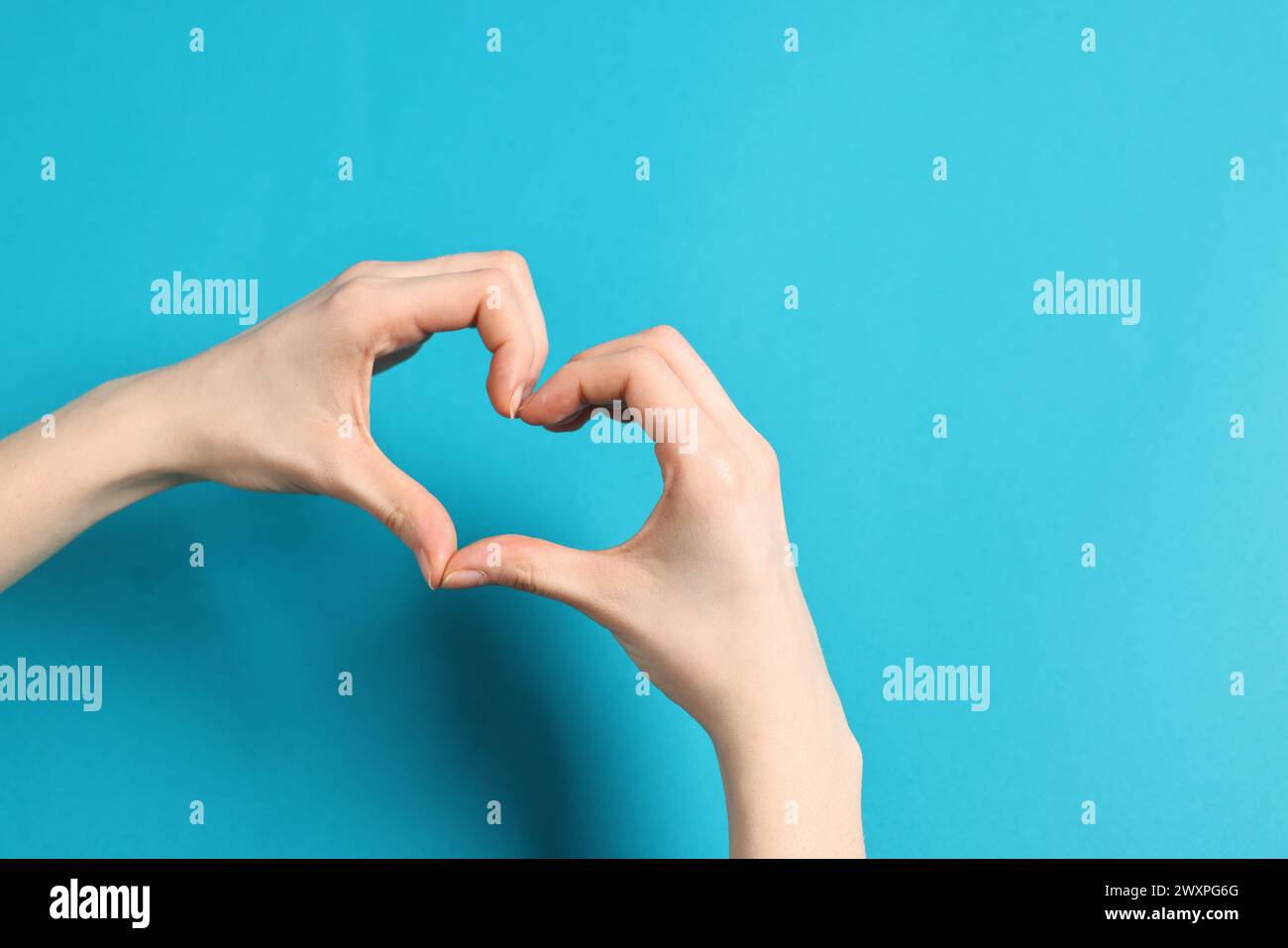Woman showing heart gesture with hands on light blue background, closeup. Space for text Stock Photo