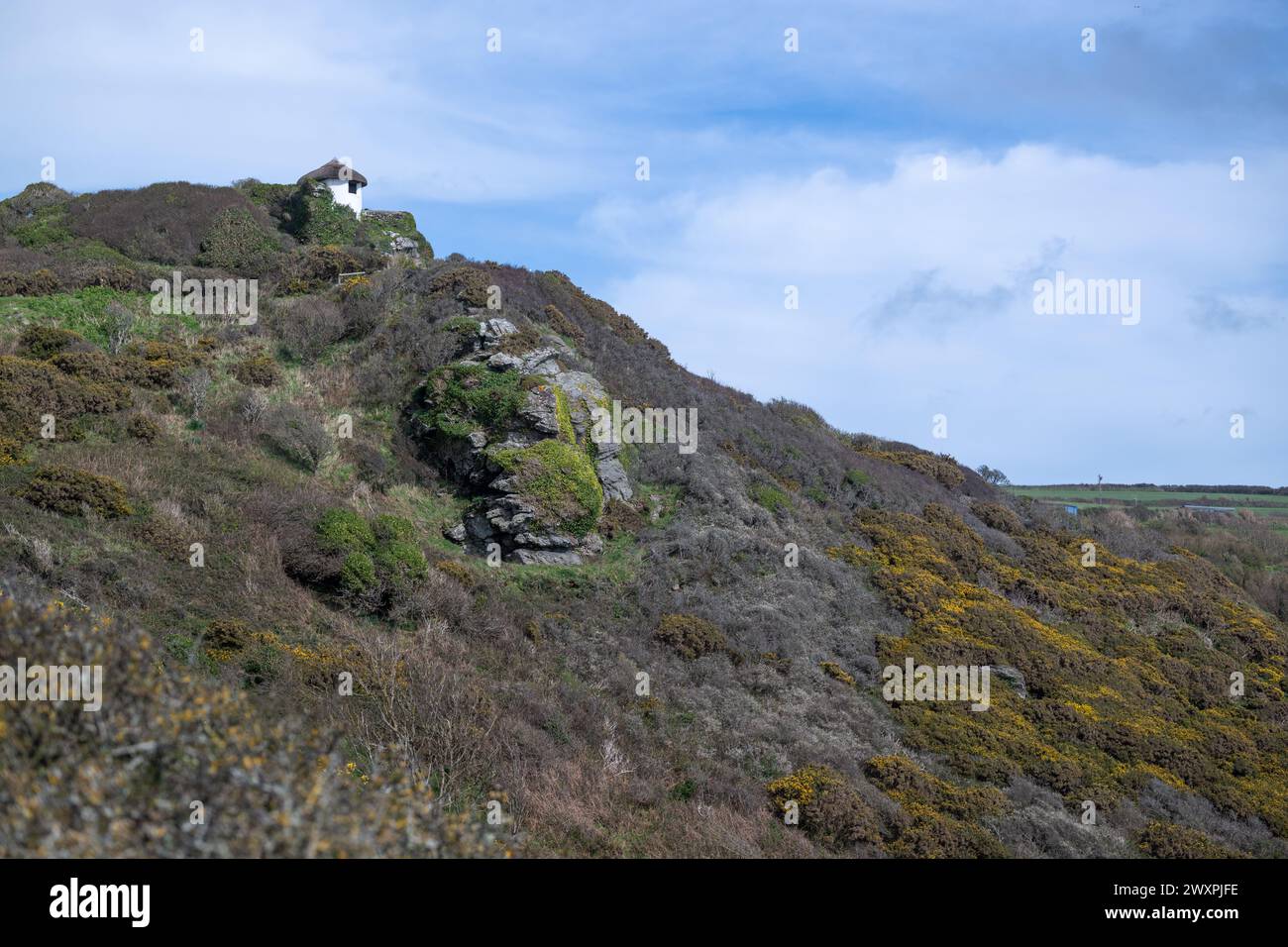 View of hut at Gara Rock hotel sitting high up on the cliff, beside SW coastal path under blue sky with big white clouds Stock Photo