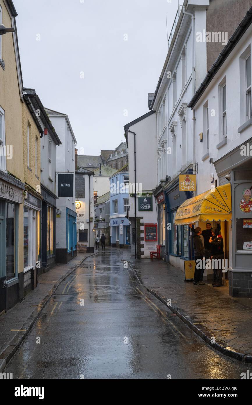 View along a wet and deserted For Street, with people standing at the Fish and Chip shop waiting and lights reflected in the puddles. Stock Photo