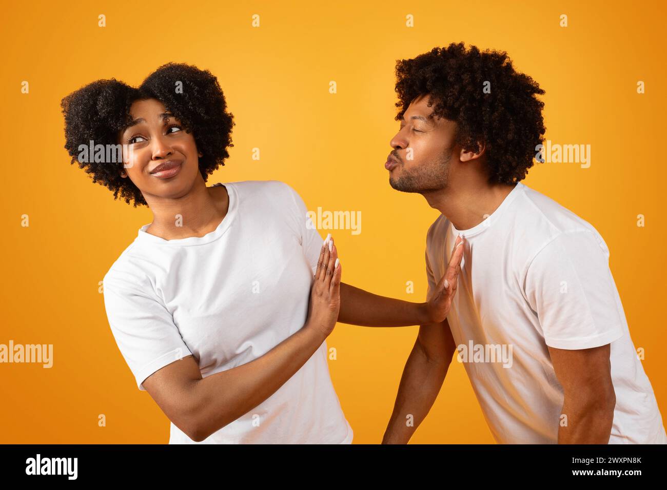 Disgusted black woman avoiding unwanted kiss from obsessed man Stock