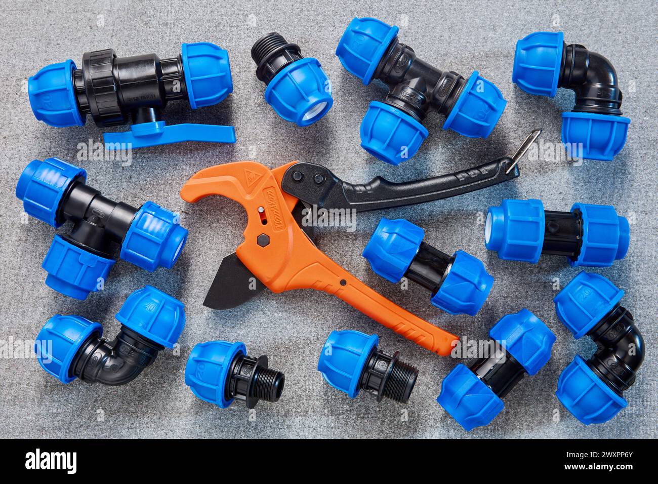 A collection of blue polyethylene pipe fittings is neatly arranged alongside an orange PVC pipe