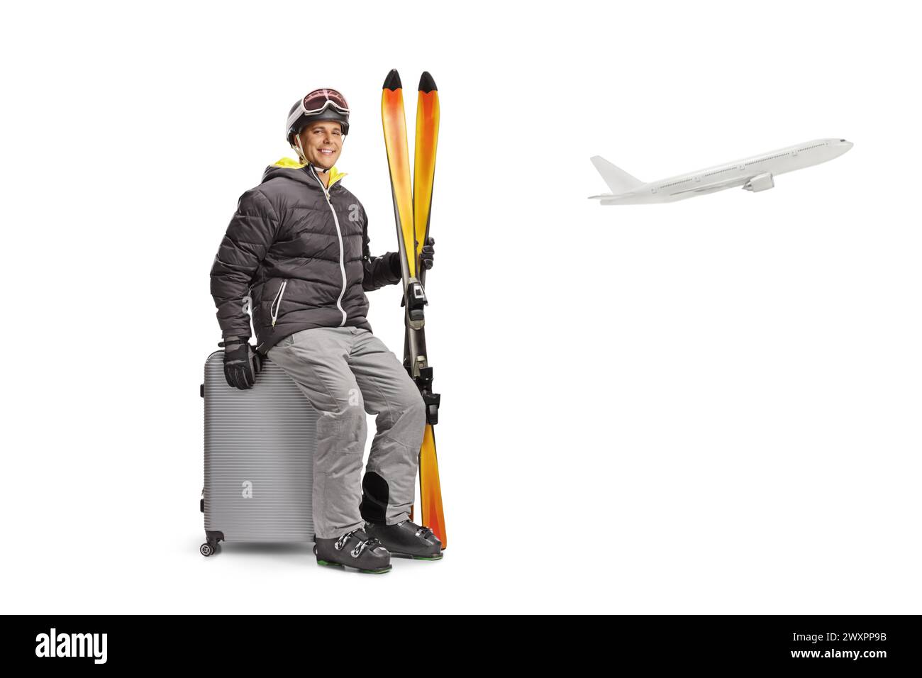 Young man with a pair of skiis sitting on a suitcase at an airport isolated on a white background Stock Photo