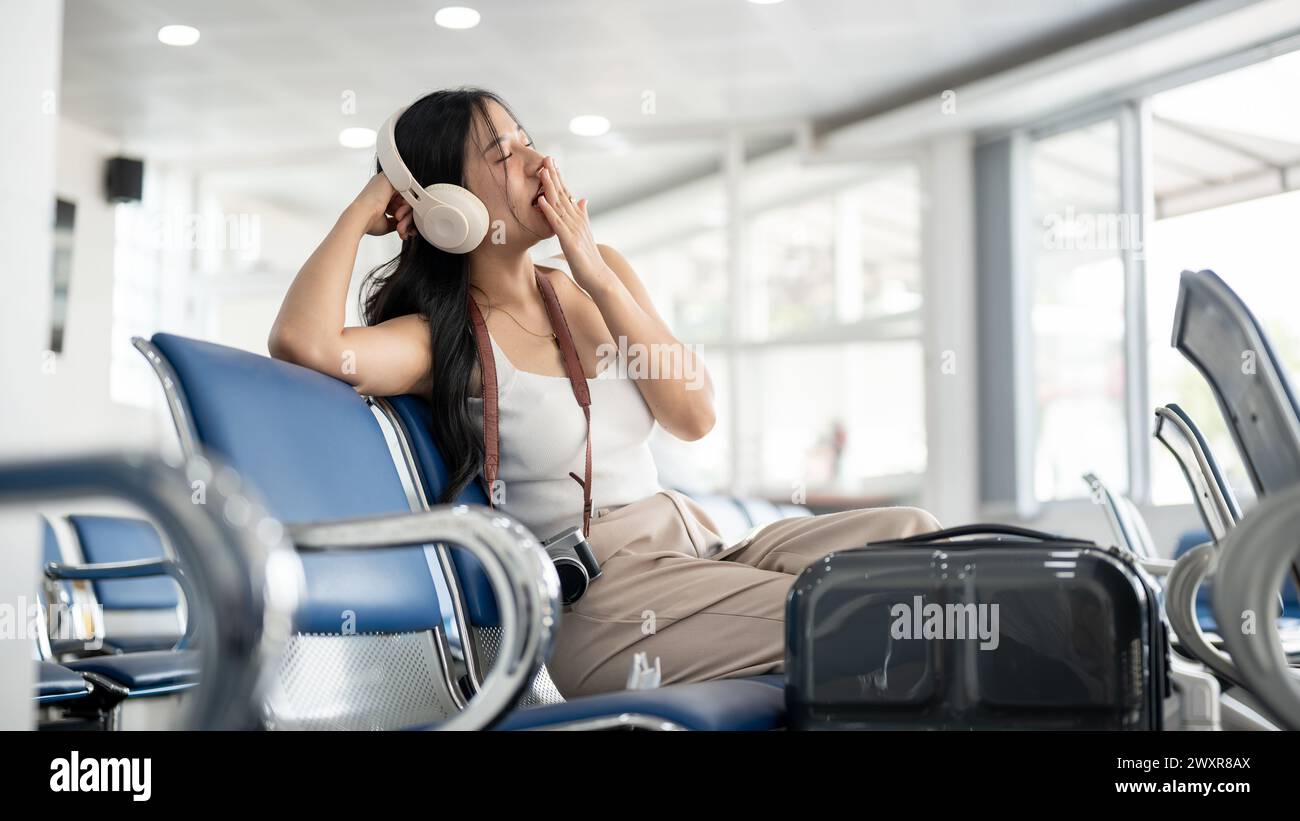 A bored and tired Asian female passenger is yawning and feeling sleepy while waiting for her flight boarding call in the airport terminal. waiting for Stock Photo
