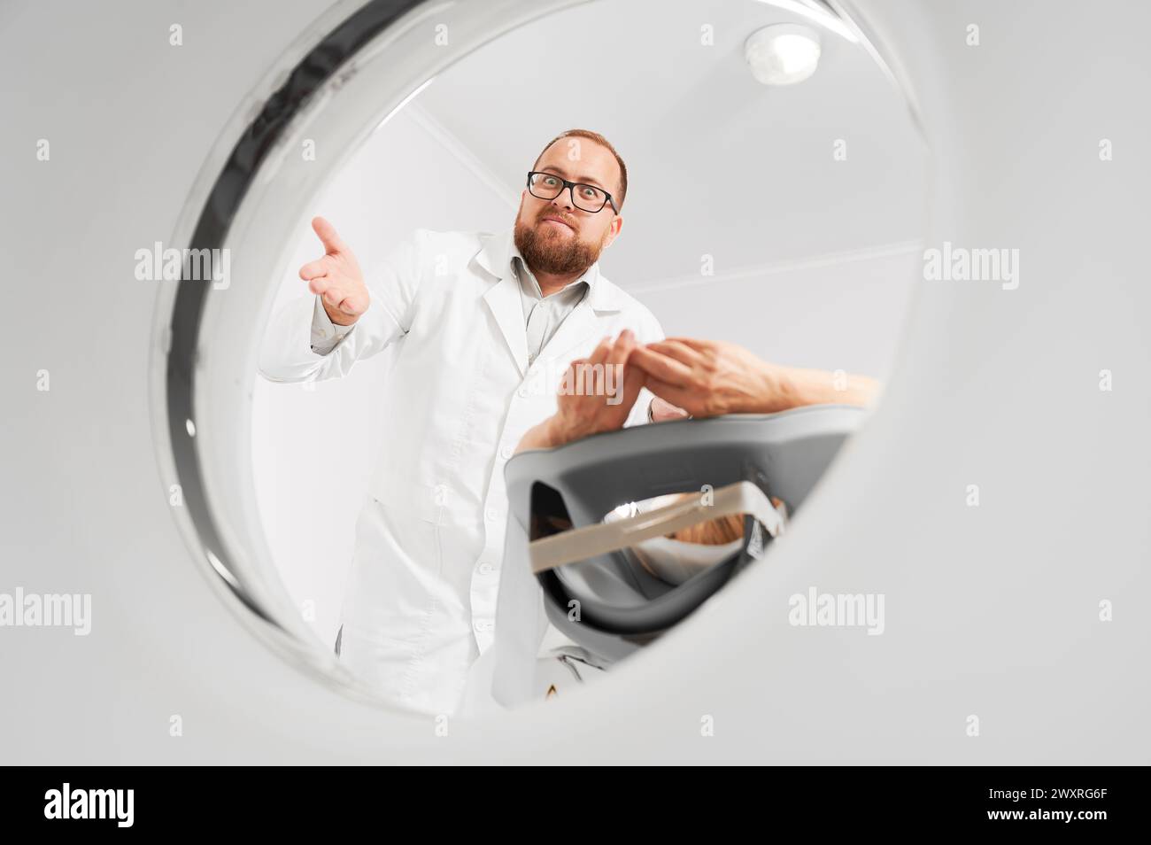 Medical computed tomography or MRI scanner. Male radiologist examine female patient, looking to the camera. Concept of modern diagnostics. Stock Photo