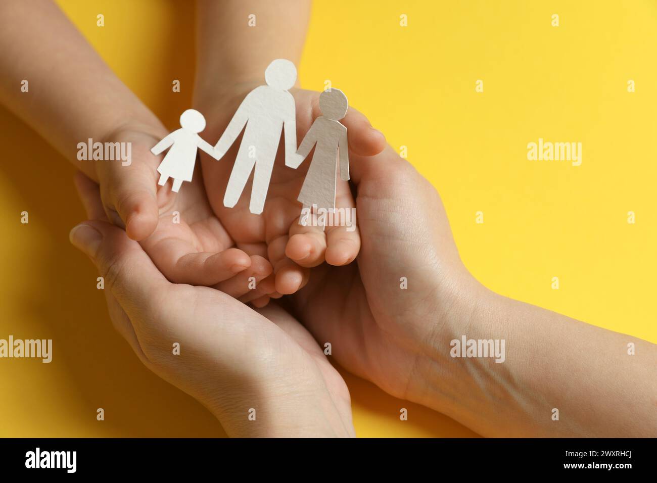 Mother and child holding paper cutout of family on yellow background, closeup Stock Photo