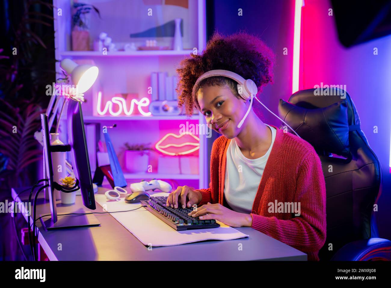 African American girl gaming streamer team winner playing online fighting with Esport wearing headphones in neon lighting room. Talking other players Stock Photo