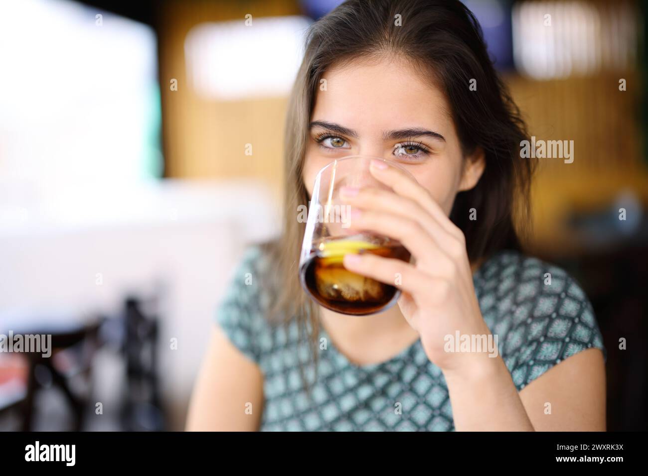 Happy woman drinking soda looking at you sitting in a bar interior Stock Photo
