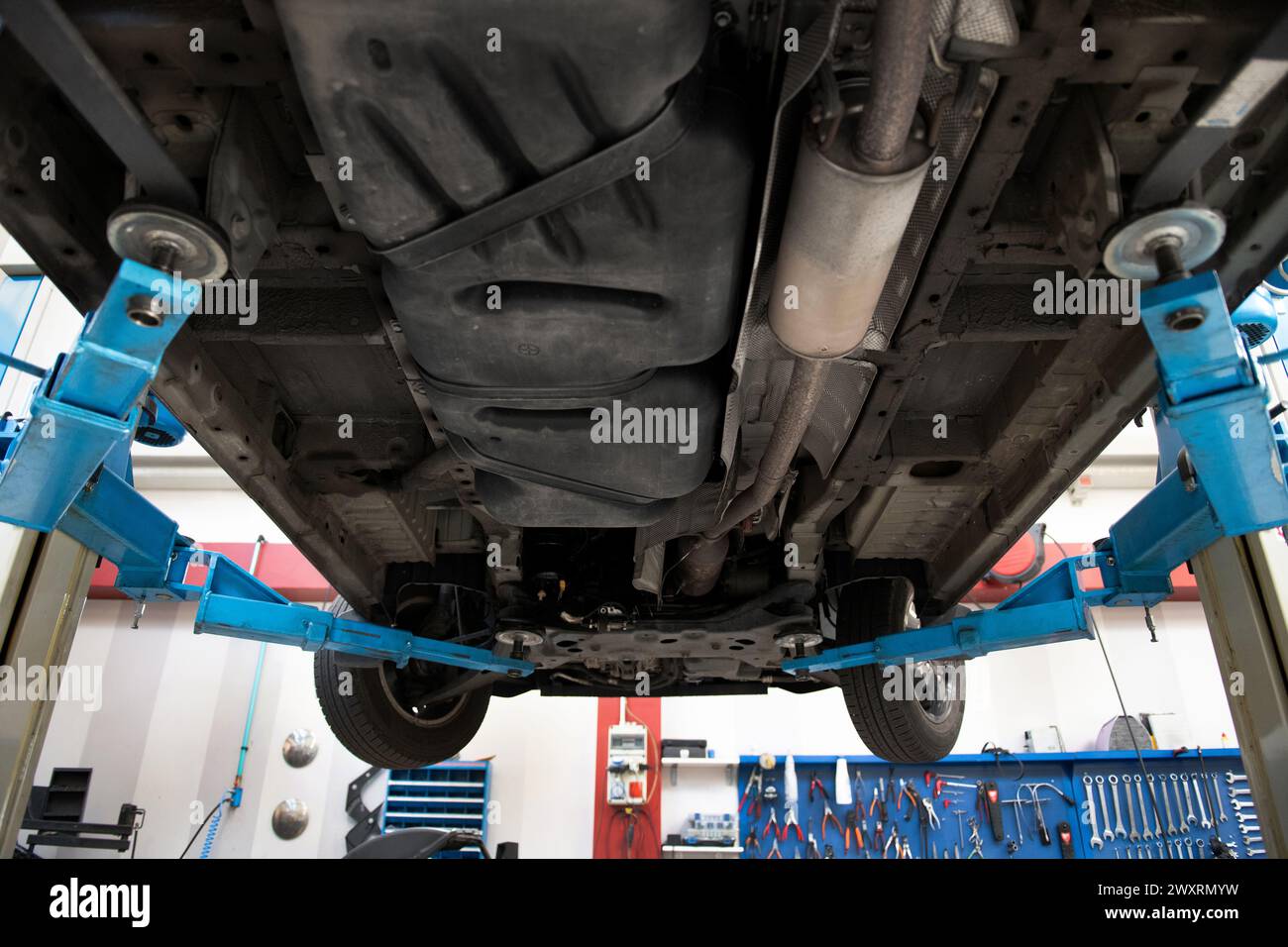 From below of lifted car bottom with exhaust system and in garage workshop for maintenance displaying parts underneath along with front wheels in dayl Stock Photo