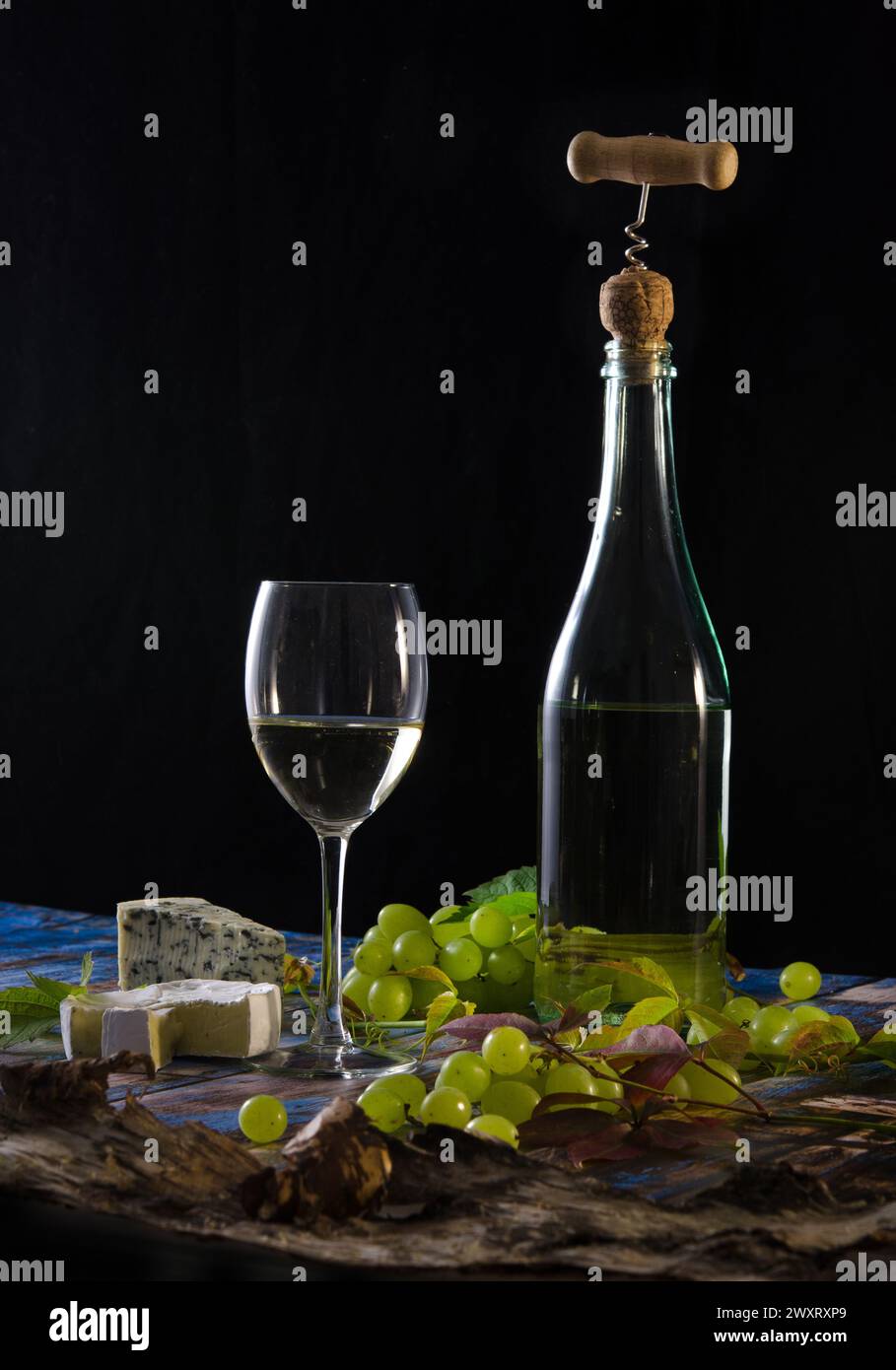 Bottle of wine with corkscrew, wineglass, ble cheese and green grapes on a black background. Stock Photo