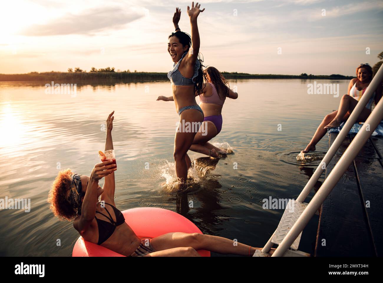 Group of female friends enjoying a summer day jumping at the lake. Stock Photo