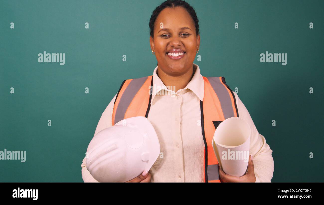 Young Black construction worker smiling holding hard hat, working on site Stock Photo