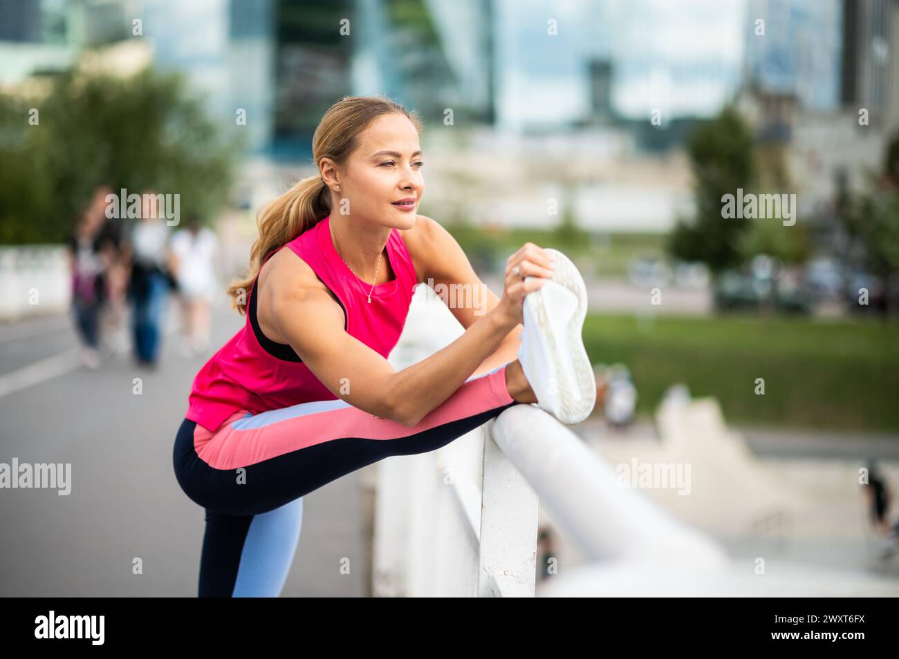 Young female runner stretching on a bridge in an urban setting Stock Photo