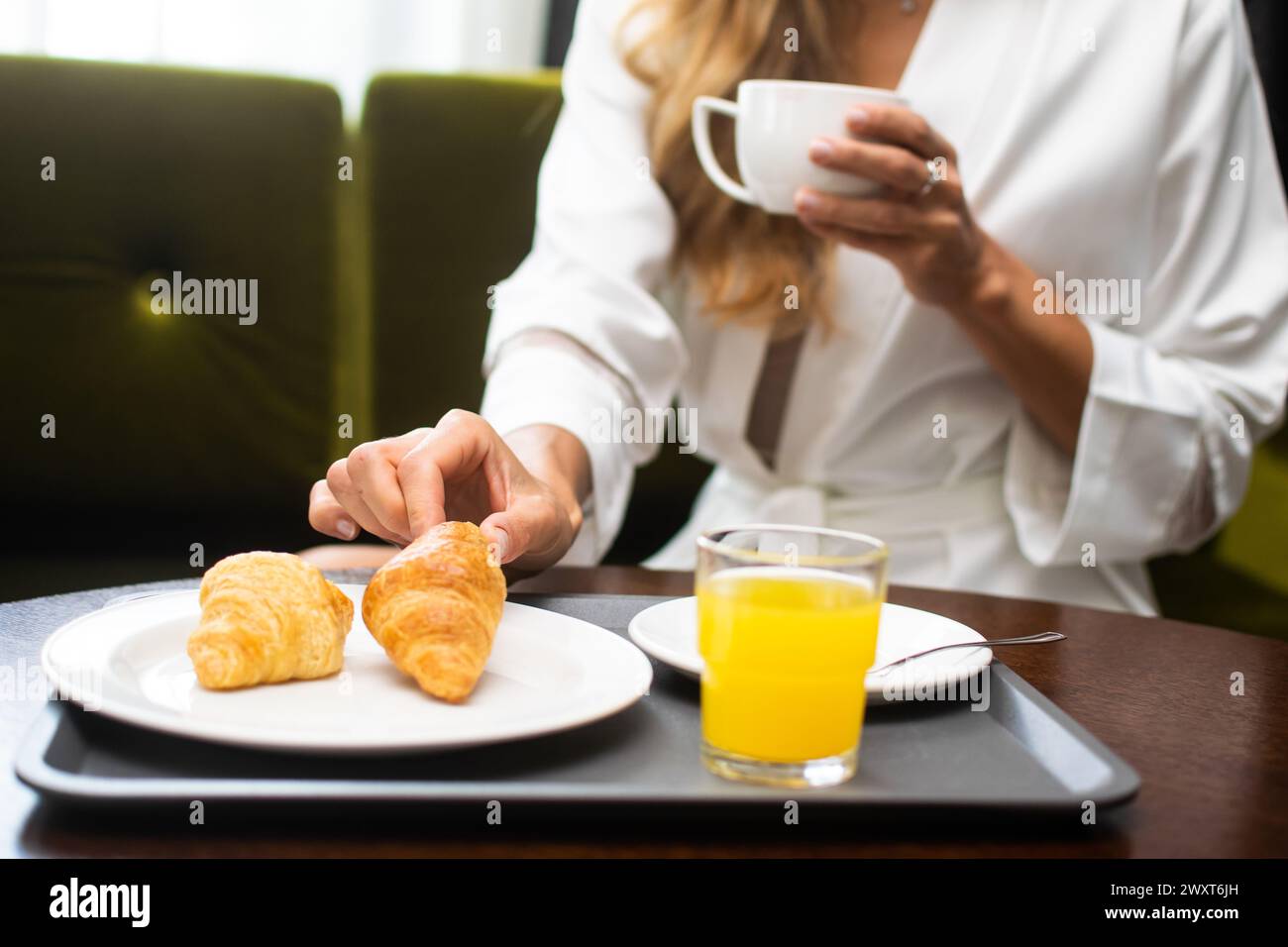 A woman sips coffee with croissants and orange juice at a cozy café. Stock Photo