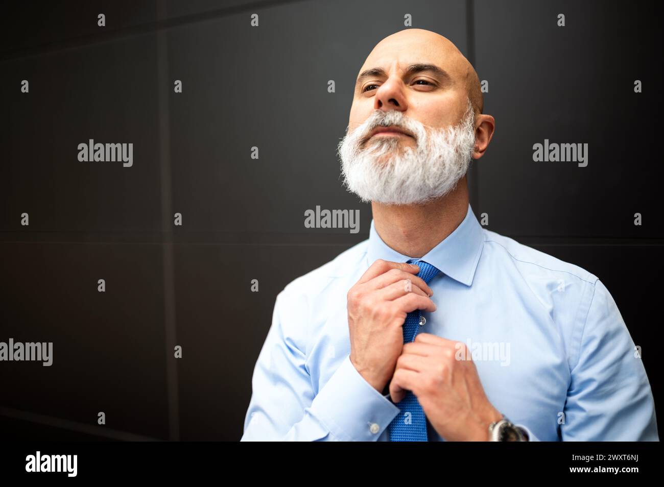 Mature bald stylish business man portrait with a white beard outdoor adjusting his necktie Stock Photo