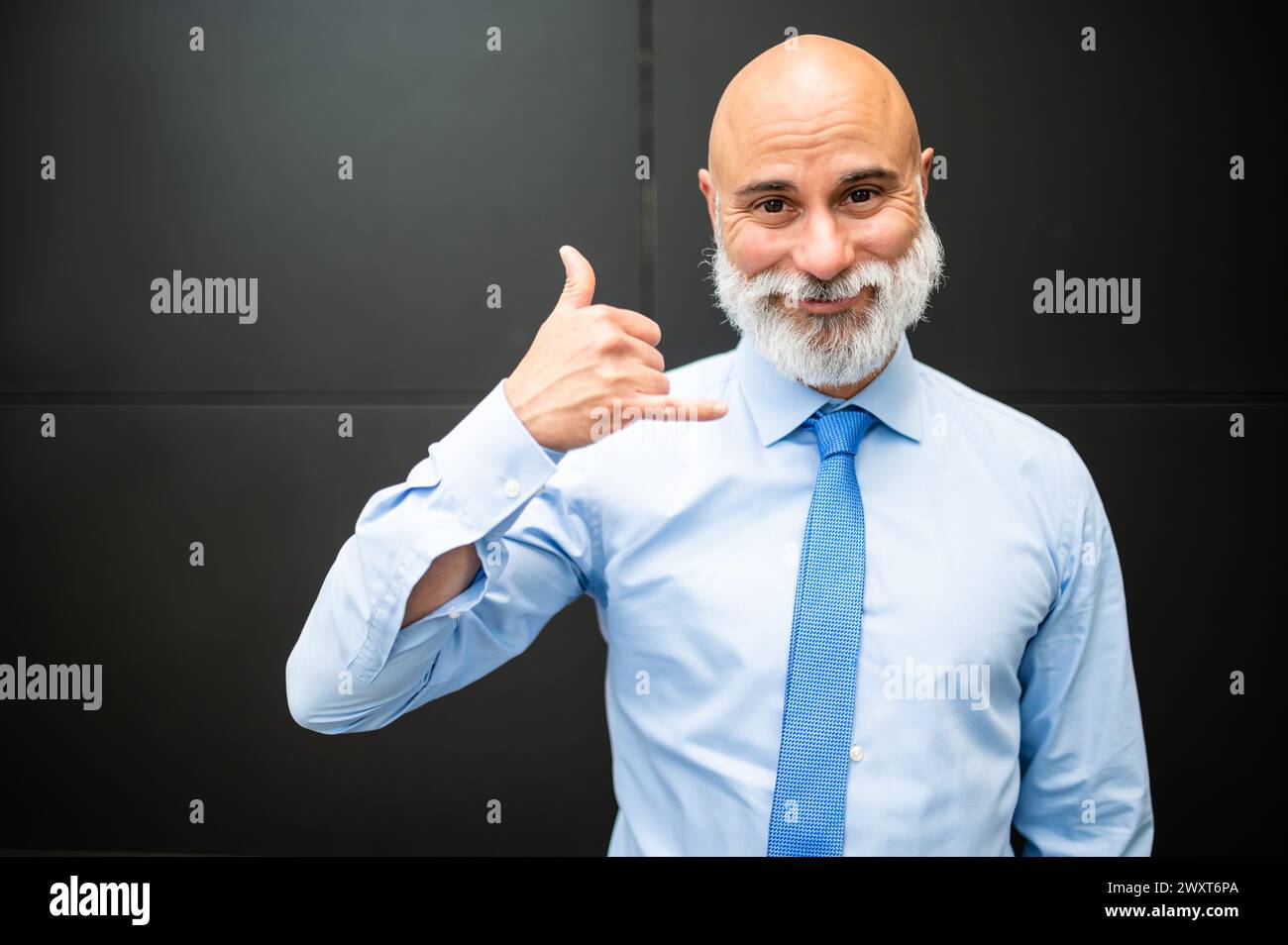 Mature bald stylish business man portrait with a white beard outdoor doing the call sign with his hand Stock Photo