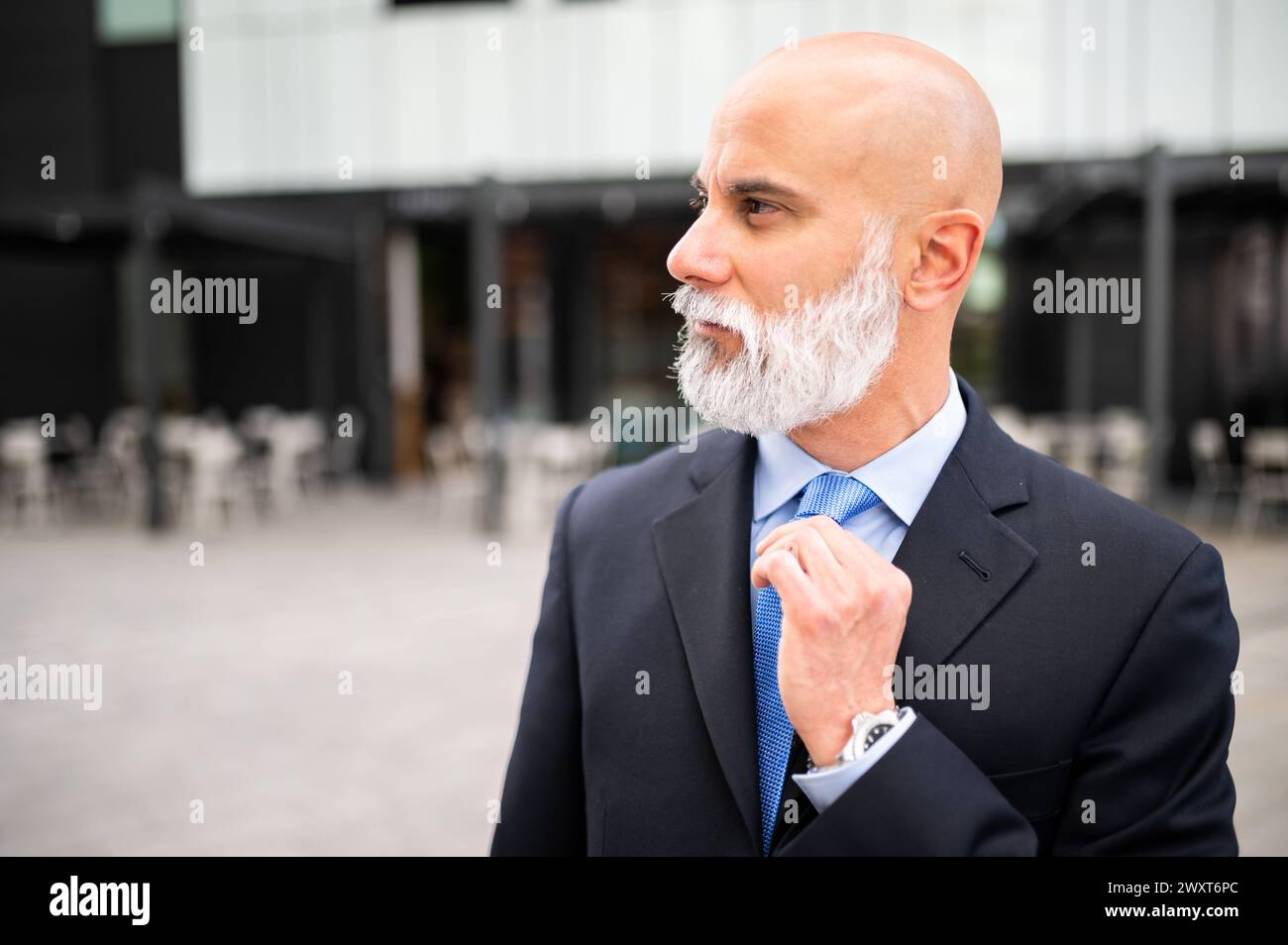 Mature bald stylish business man portrait with a white beard outdoor adjusting his necktie Stock Photo