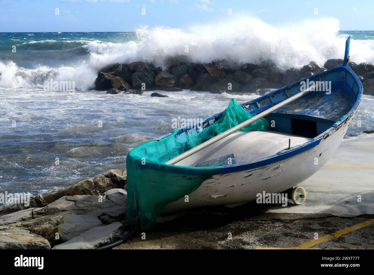 A boat rests on the shore near a rocky ledge as waves crash in the distance Stock Photo