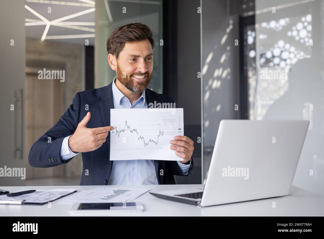 A cheerful businessman in a modern office presenting a graph during a ...