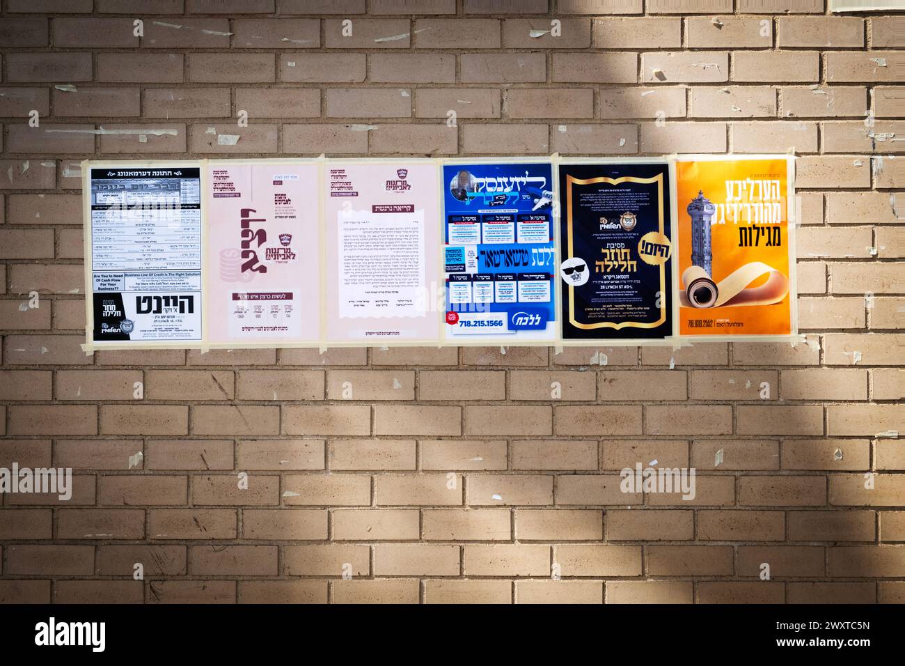 6 posters primarily in ornate Yiddish calligraphy, taped to a wall on a de facto community bulletin board. On Williamsburg St West in Brooklyn, N. Stock Photo