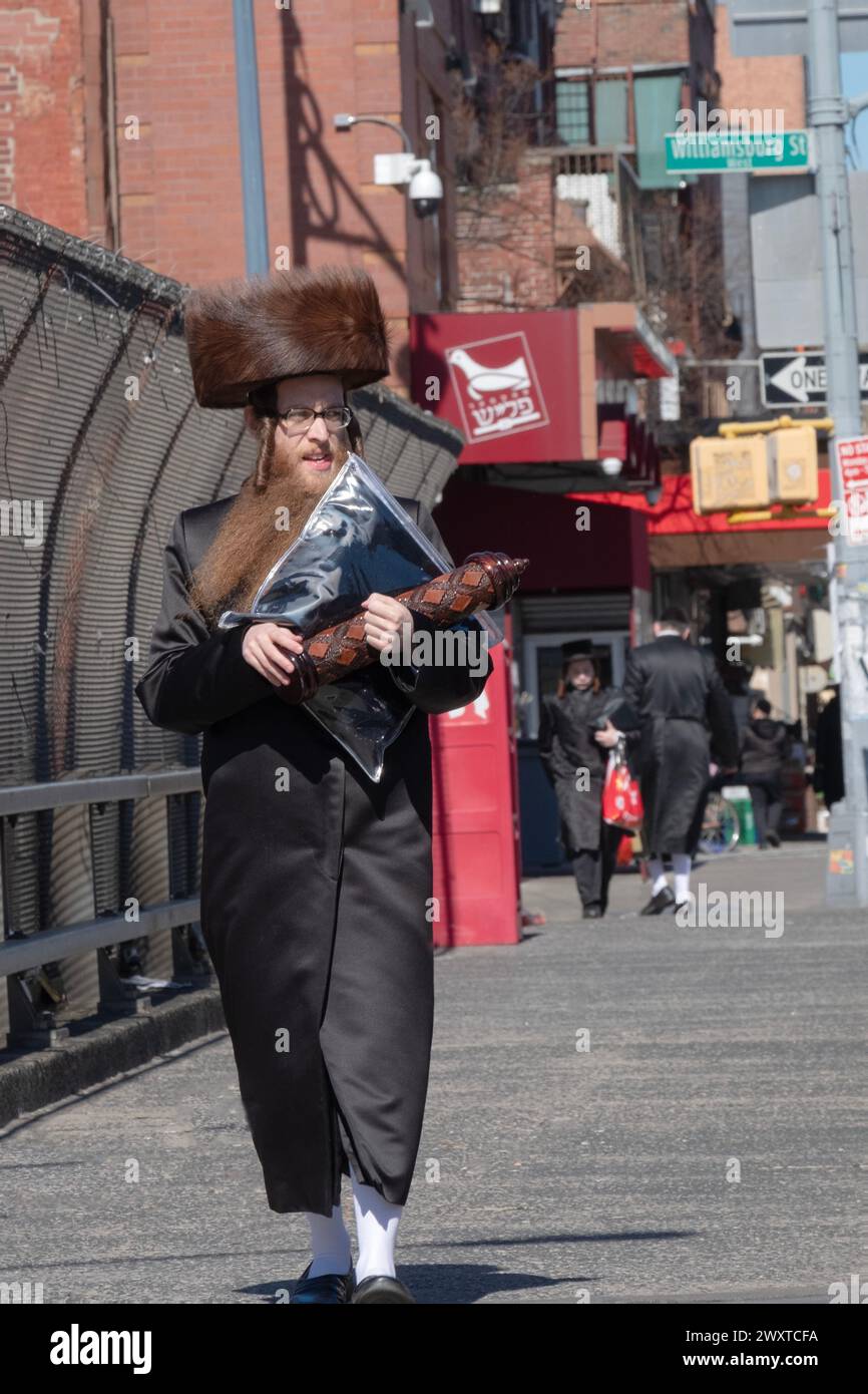 An orthodox Jewish man returns from temple on Purim wearing a shtreimel fur hat and carrying a tallis bag & megillah. In Brooklyn, New York. Stock Photo