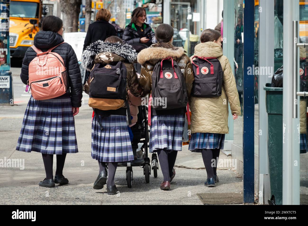 Four  orthodox Jewish girls in identical skirts walk together  in Brooklyn, New York. They are classmates in their school uniforms. Stock Photo