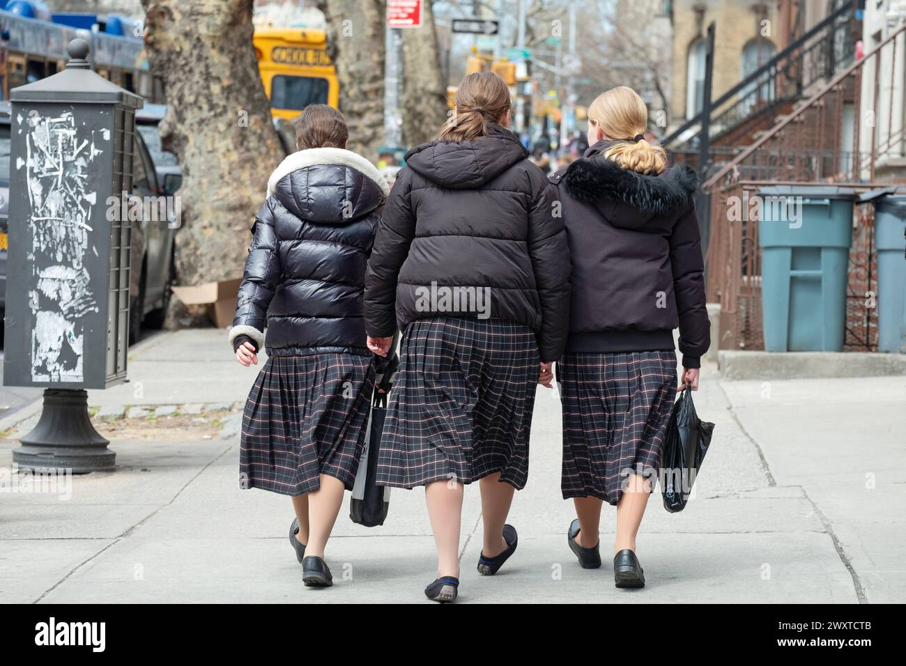 Three  orthodox Jewish girls in identical skirts walk closely together  in Brooklyn, New York. They are classmates in school uniforms. Stock Photo