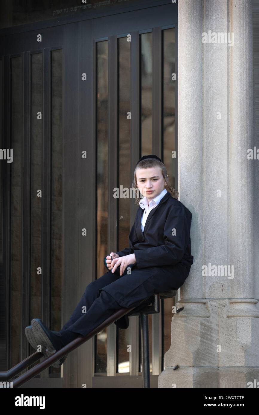 During recess at his yeshiva, an orthodox Jewish student is lost in thought while taking an impromptu seat on a stair bannister. In Brooklyn, NY Stock Photo