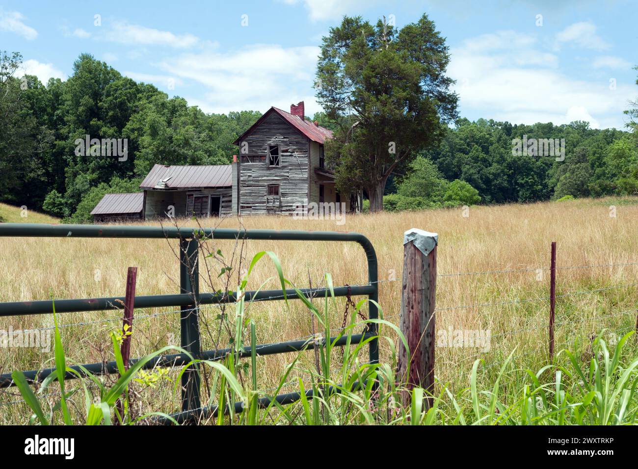 Old rustic wooden barn in a field with trees in the background.  Closed gate, fence and post in the foreground.  Near Asheville, North Carolina. Stock Photo