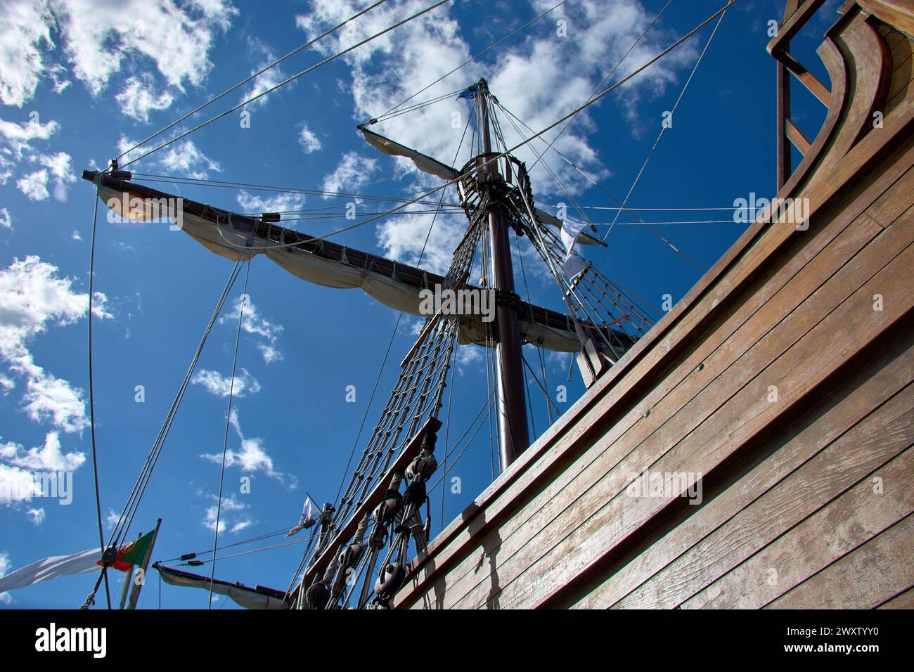 The tall wooden masts of the replica caravel Santa Maria against a clear blue sky with some cloud. Many tightrope rigging and rope ladders are seen. B Stock Photo