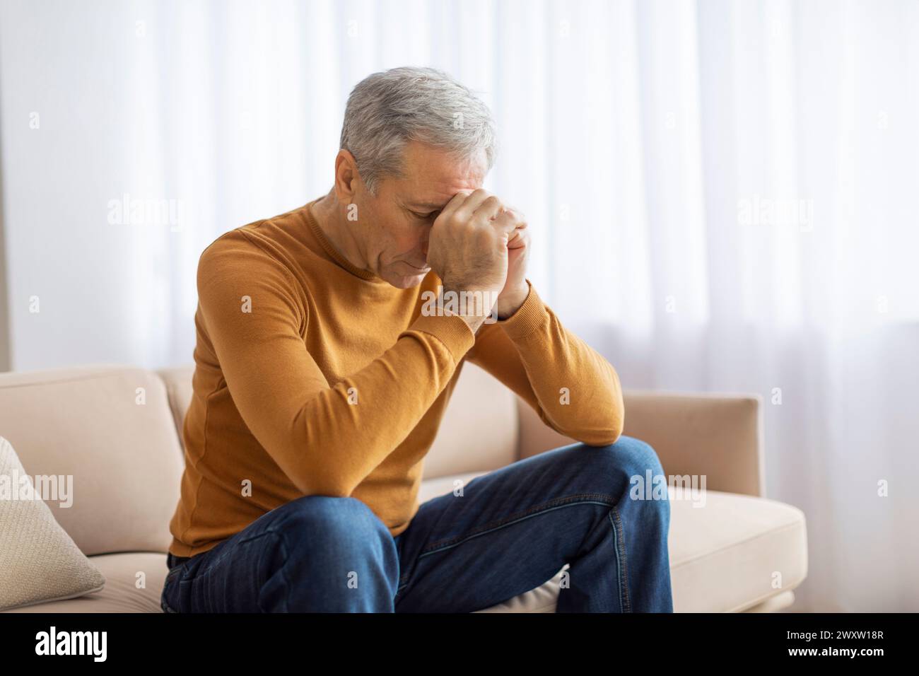 Elderly man sitting on sofa with head resting on hand Stock Photo