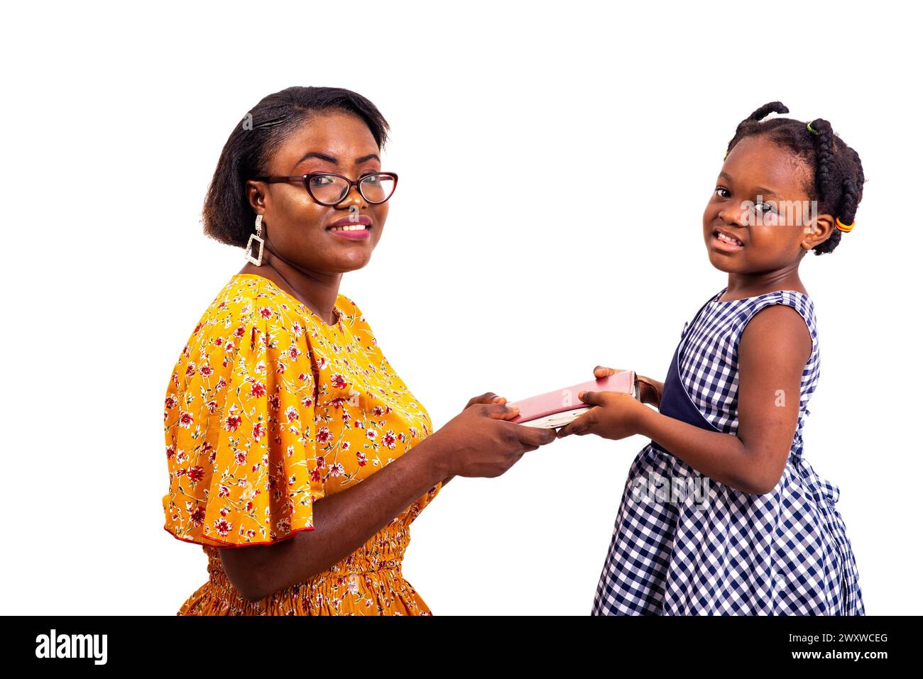 a charming businesswoman in glasses kneeling on white background giving a book to her smiling daughter. Stock Photo