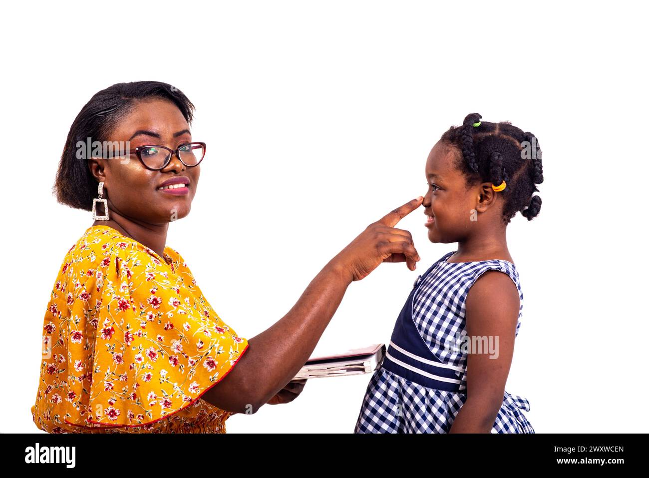 a charming businesswoman in glasses kneeling on white background touching her schoolgirl daughter's nose while smiling. Stock Photo