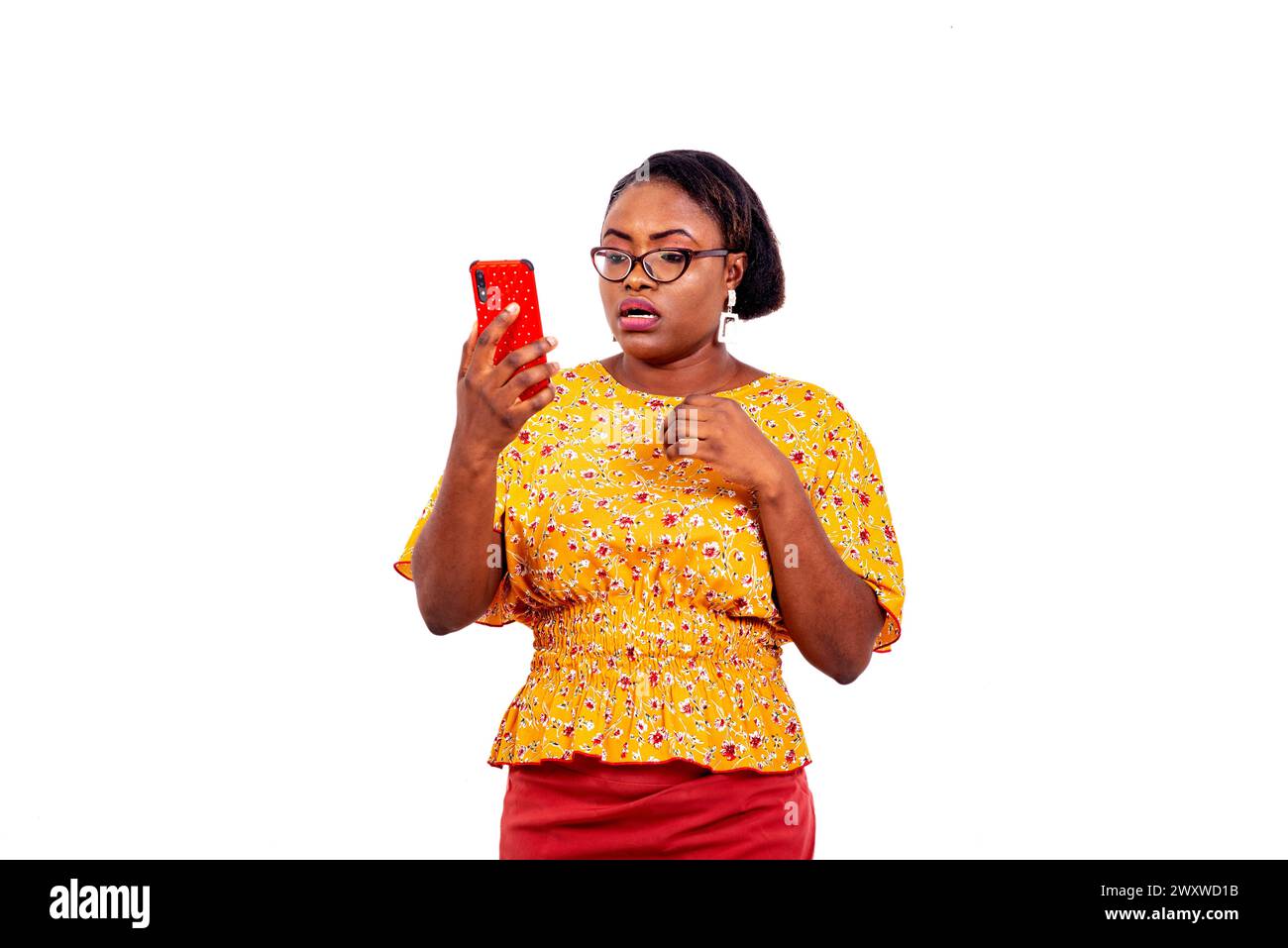 a beautiful businesswoman in eyeglasses standing over white background looking at cellphone with surprised look. Stock Photo