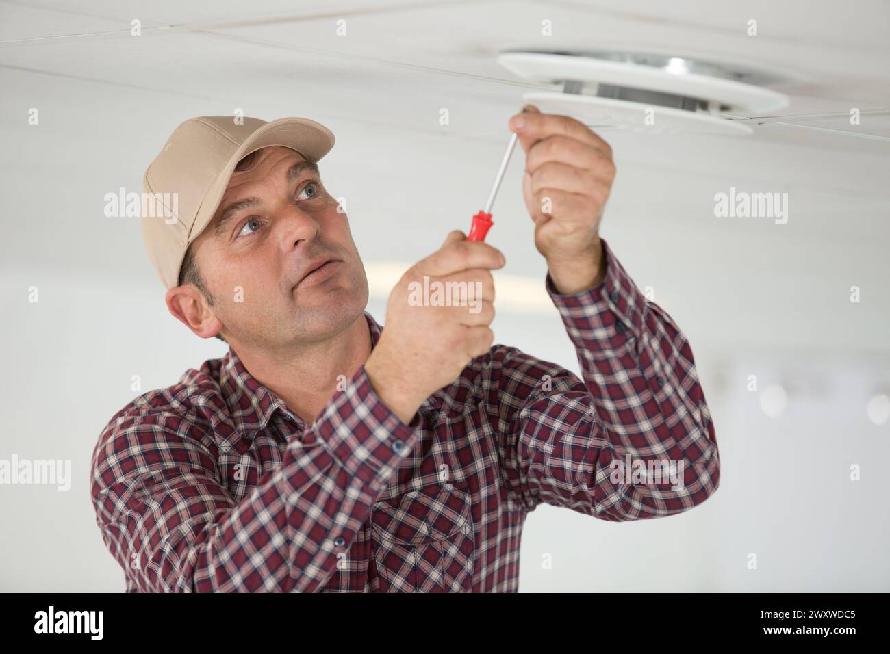 a workman is securing screws on ceiling Stock Photo