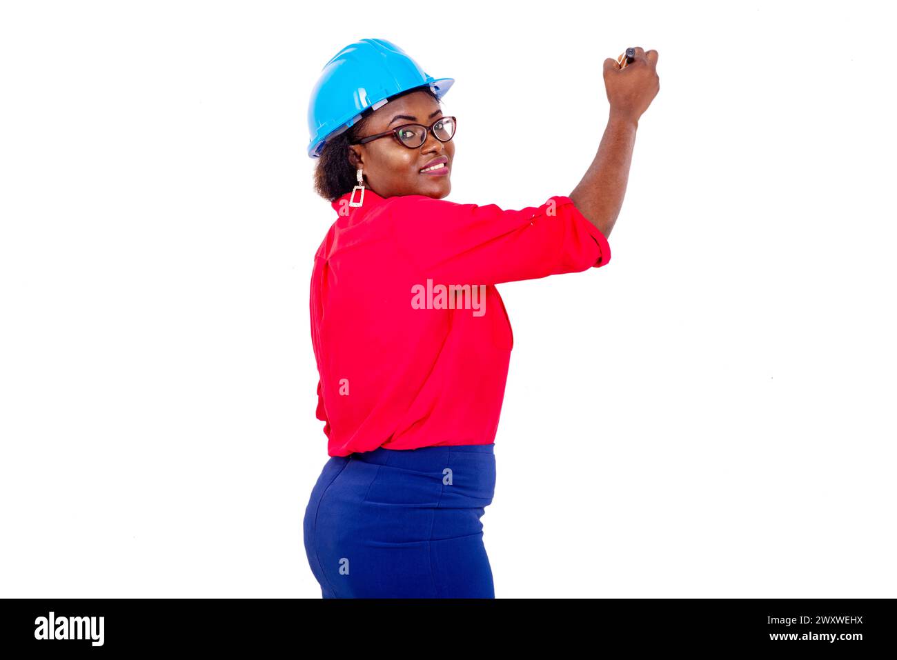 beautiful adult female engineer wearing blue safety helmet writing on a whiteboard with a mark while smiling. Stock Photo