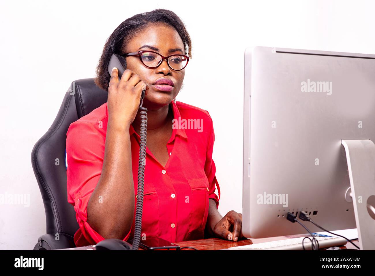 beautiful adult business woman wearing optical glasses sitting at desk and talking on mobile phone. Stock Photo