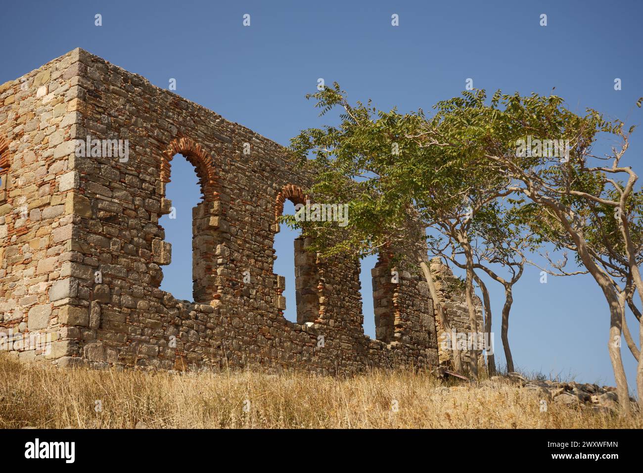 Ruins of a roofless stone building with three big windows stand next to a group of trees in Myrina castle, Lemnos island, Greece Stock Photo