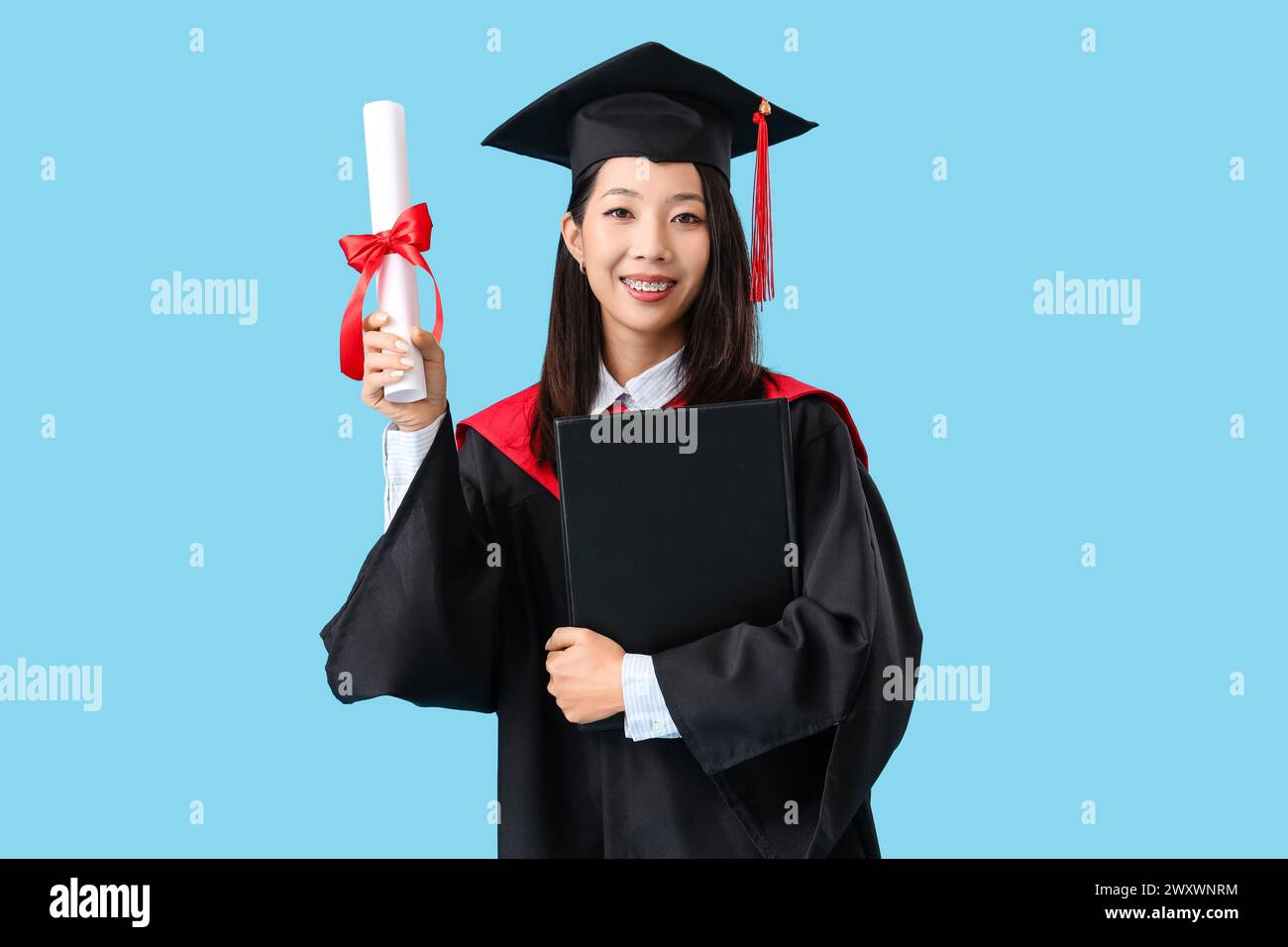 Asian female graduate student with diploma and book on blue background Stock Photo