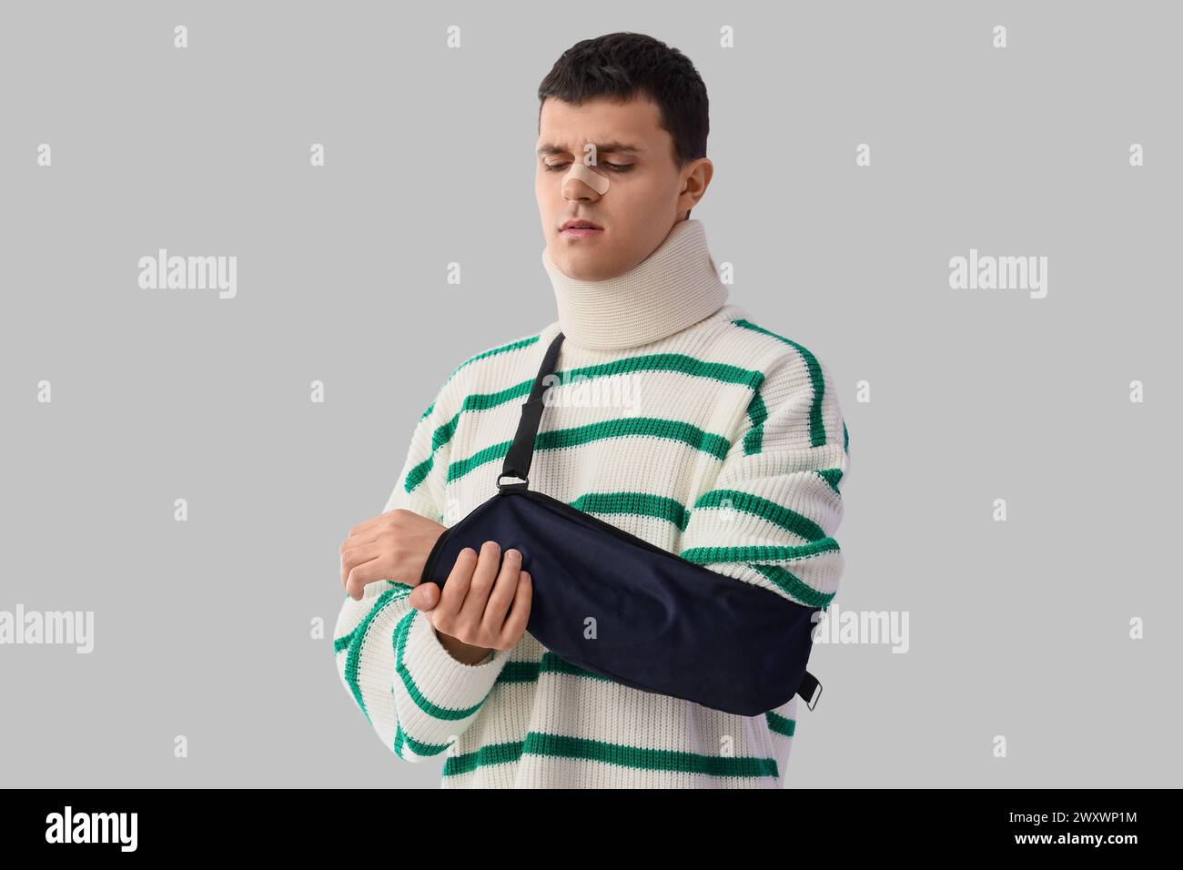 Injured young man after accident with broken arm on light background Stock Photo