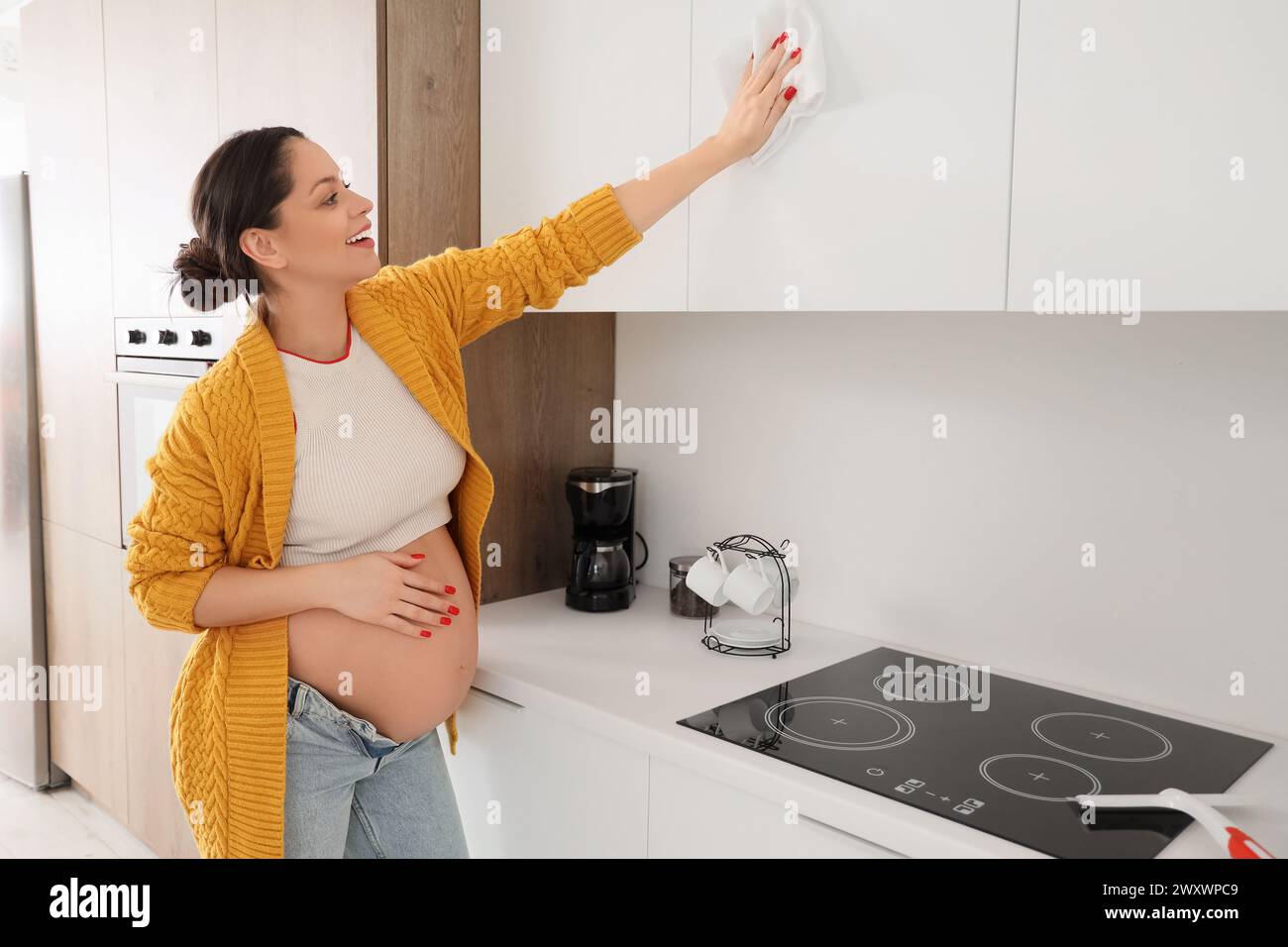 Young pregnant woman cleaning cupboard in kitchen Stock Photo