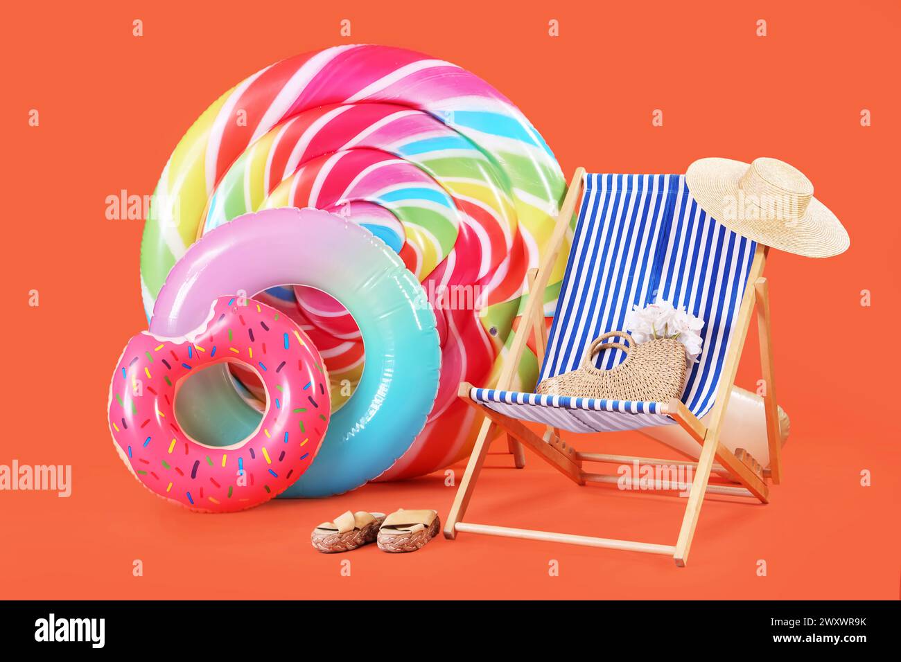 Swimming mattress in shape of candy, inflatable rings and sun lounger with straw hat on orange background Stock Photo