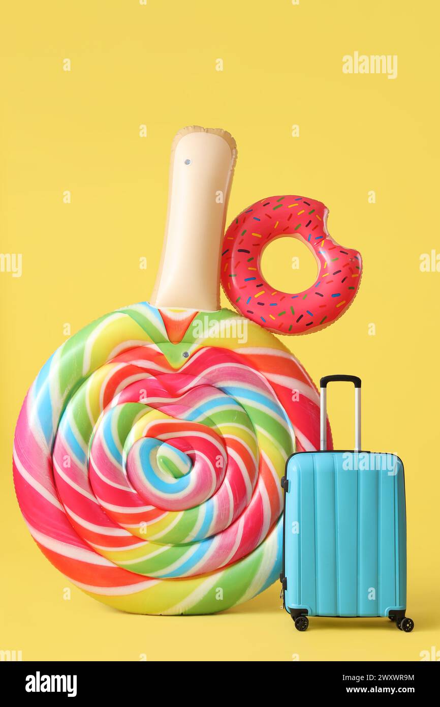 Swimming mattress in shape of candy, inflatable ring and suitcase on yellow background Stock Photo