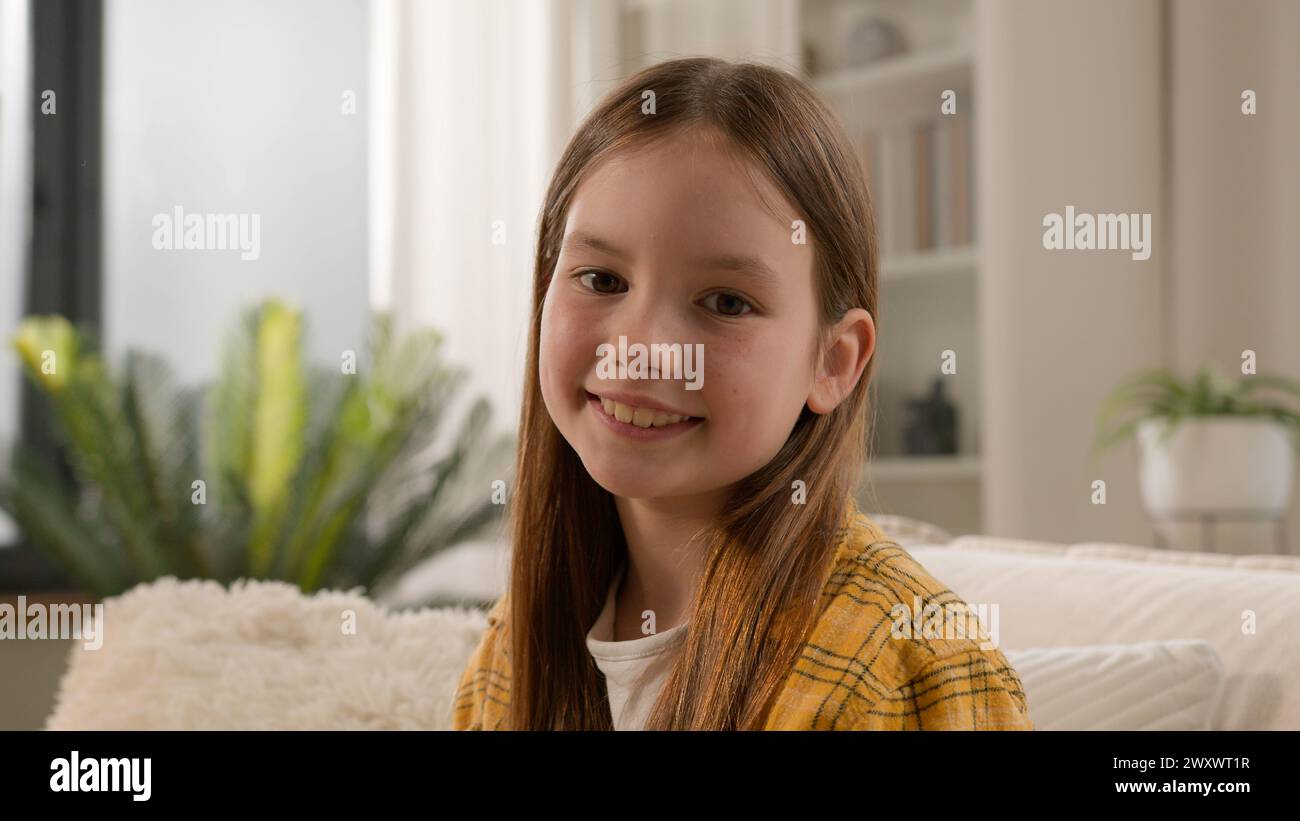 Portrait funny cute satisfied caucasian kid girl looking at camera in living room smiling toothy smile positive preteen child schoolgirl with pretty Stock Photo